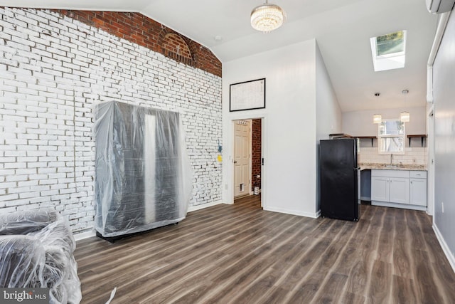 kitchen with vaulted ceiling with skylight, dark wood-style floors, brick wall, open floor plan, and freestanding refrigerator