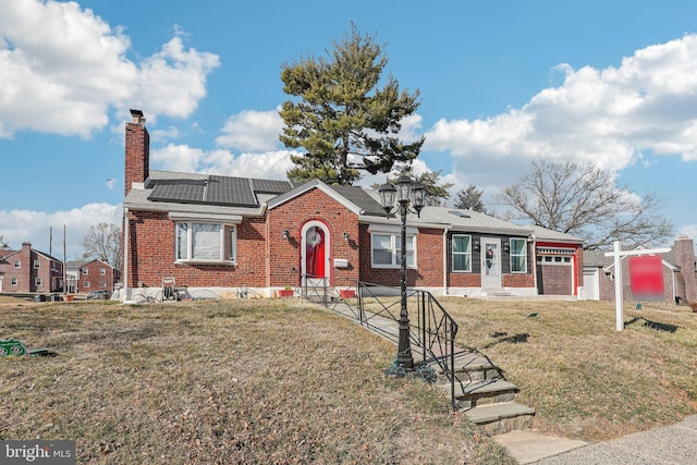 view of front of home with brick siding, a chimney, an attached garage, roof mounted solar panels, and a front yard