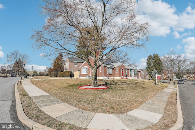 view of front of property featuring a residential view, roof mounted solar panels, brick siding, and a front lawn