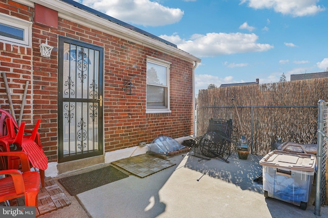 view of exterior entry with fence, a patio, and brick siding