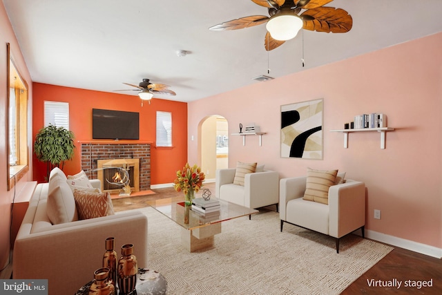 living area with arched walkways, a fireplace, visible vents, ceiling fan, and baseboards