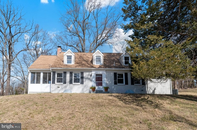 new england style home featuring a front lawn, brick siding, a sunroom, and a chimney