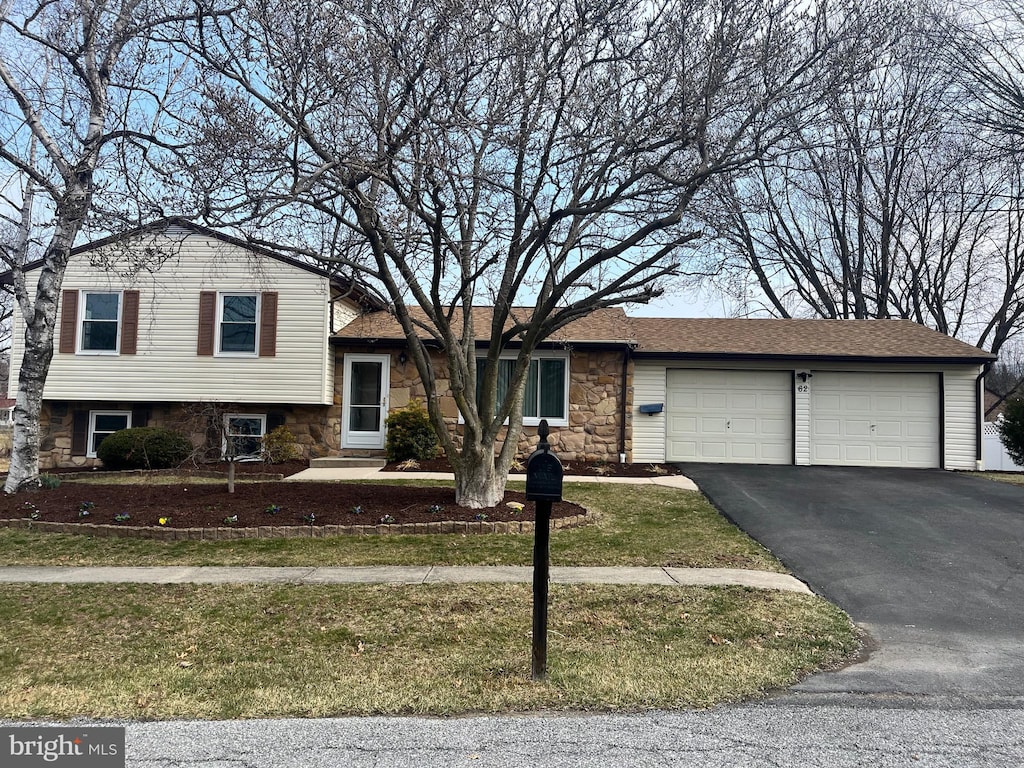 split level home with stone siding, an attached garage, driveway, and roof with shingles