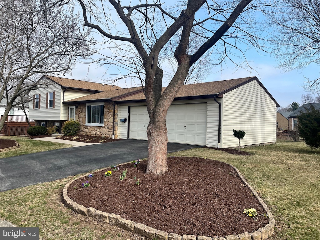 tri-level home featuring a shingled roof, a front yard, a garage, stone siding, and driveway