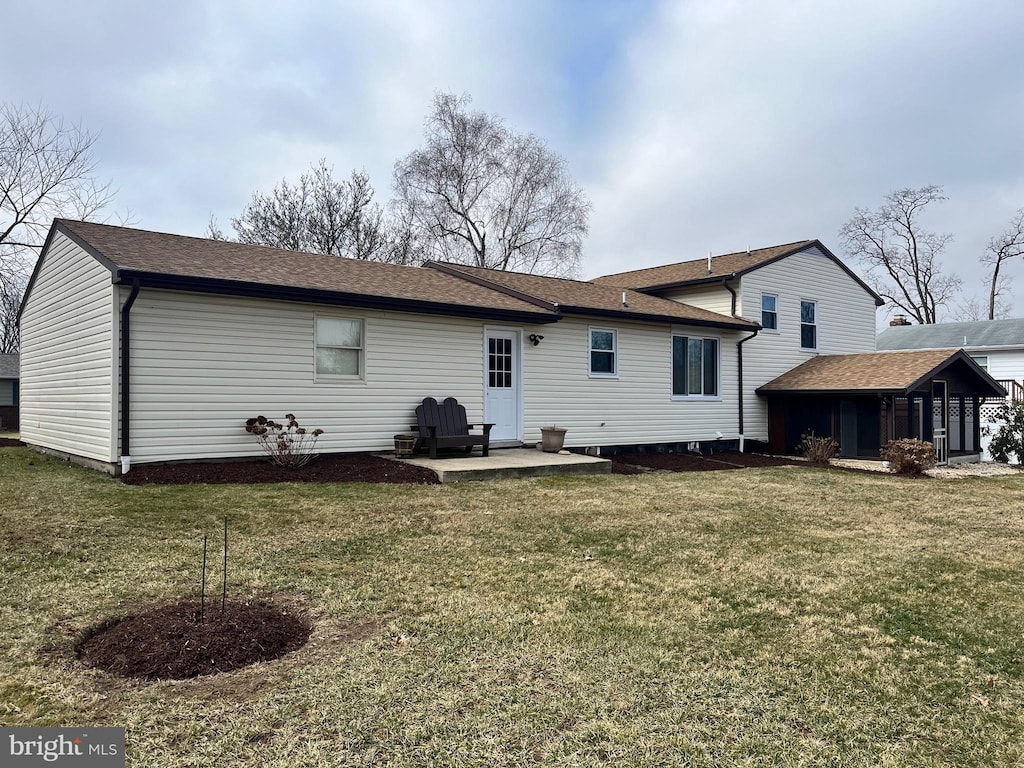 back of house with a lawn, a shingled roof, and a patio