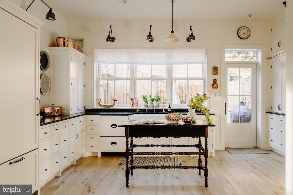 kitchen with hanging light fixtures, dark countertops, light wood-style flooring, and white cabinets