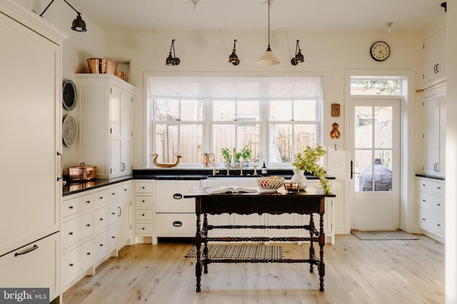 kitchen with hanging light fixtures, dark countertops, light wood-style flooring, and white cabinets