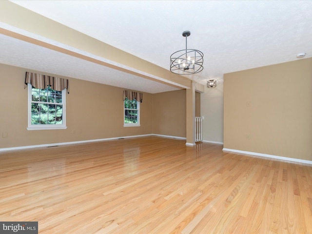 unfurnished room featuring baseboards, light wood finished floors, a wealth of natural light, and an inviting chandelier