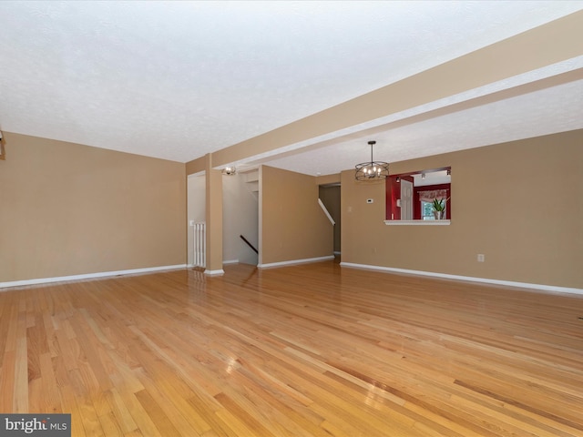 unfurnished living room featuring an inviting chandelier, light wood-style flooring, baseboards, and a textured ceiling