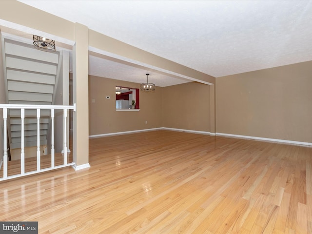 spare room featuring a textured ceiling, a notable chandelier, wood finished floors, and baseboards