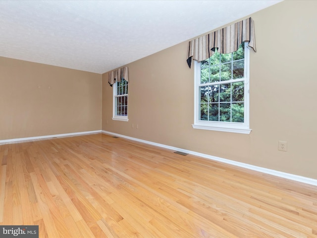 empty room with light wood-type flooring, visible vents, a textured ceiling, and baseboards