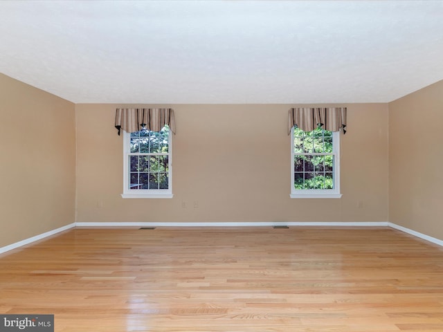 empty room with light wood-type flooring, visible vents, baseboards, and a wealth of natural light