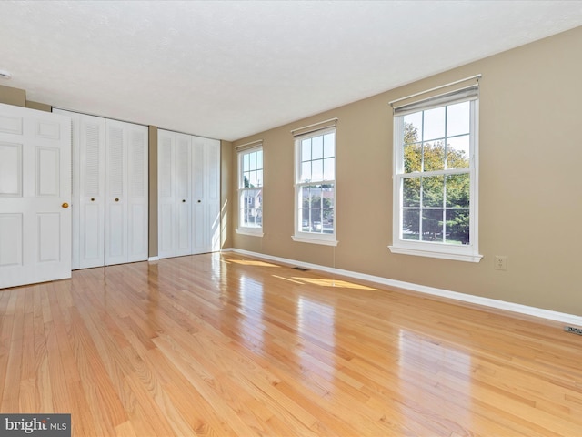 unfurnished bedroom featuring multiple closets, visible vents, baseboards, and wood finished floors