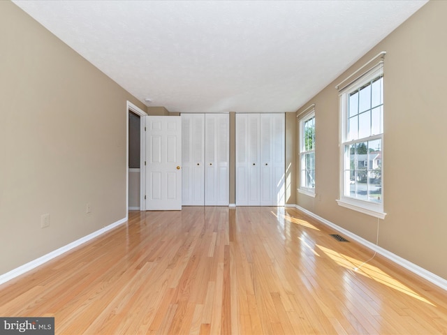 unfurnished bedroom with light wood-style flooring, baseboards, and two closets