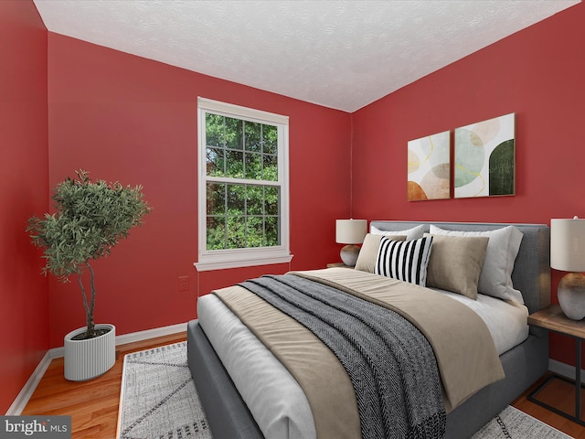 bedroom with a textured ceiling, baseboards, and wood finished floors