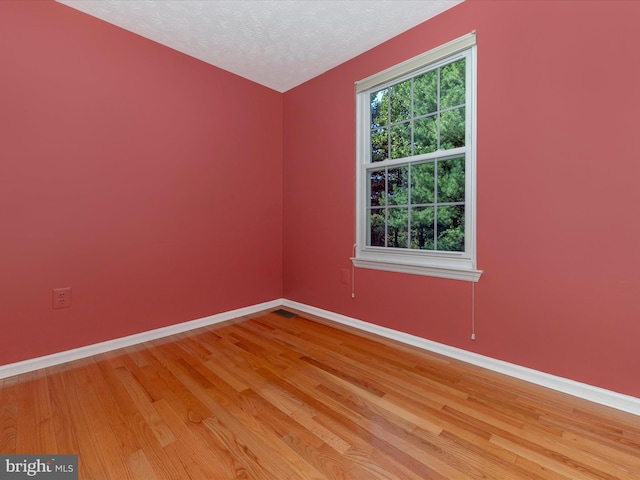 empty room with a textured ceiling, light wood-style floors, and baseboards