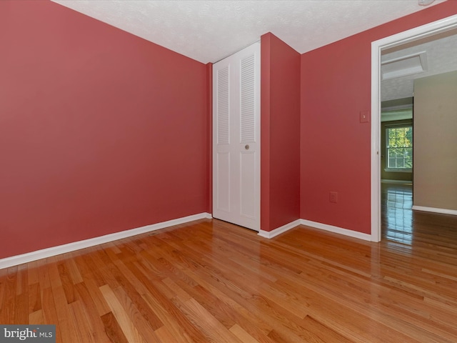 unfurnished bedroom with light wood-style floors, a closet, a textured ceiling, and baseboards