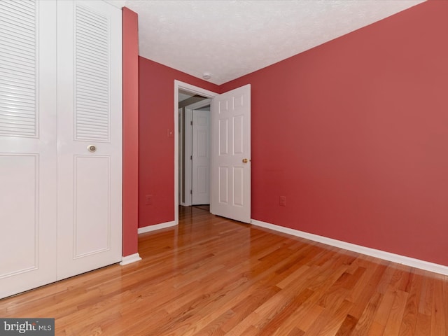 unfurnished bedroom with light wood-style floors, a closet, a textured ceiling, and baseboards