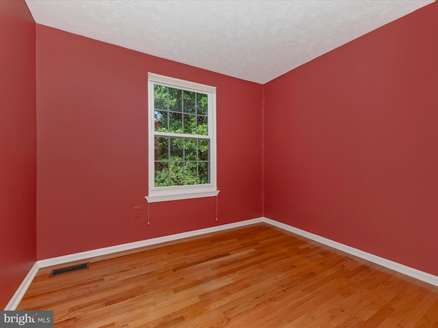 empty room with light wood finished floors, visible vents, baseboards, and a textured ceiling