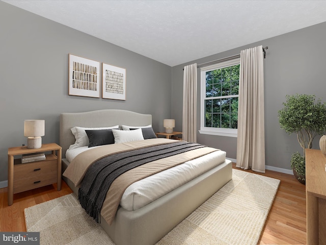 bedroom featuring a textured ceiling, light wood-style flooring, and baseboards