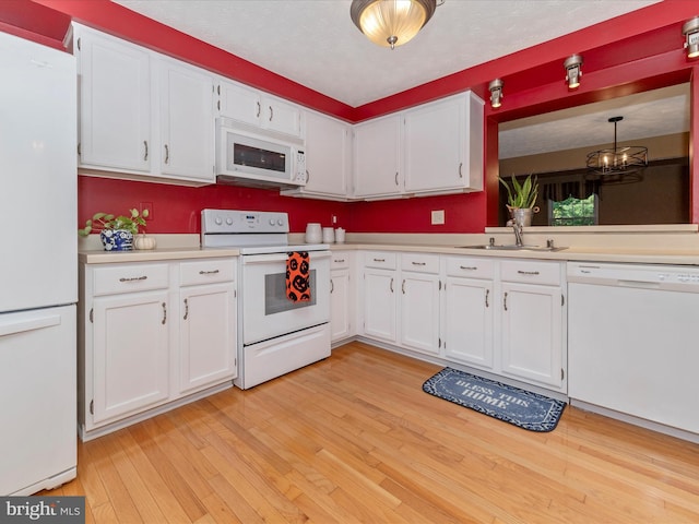 kitchen with white appliances, a sink, white cabinets, light wood-style floors, and light countertops