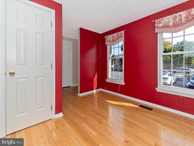 spare room with hardwood / wood-style flooring, baseboards, visible vents, and a textured ceiling