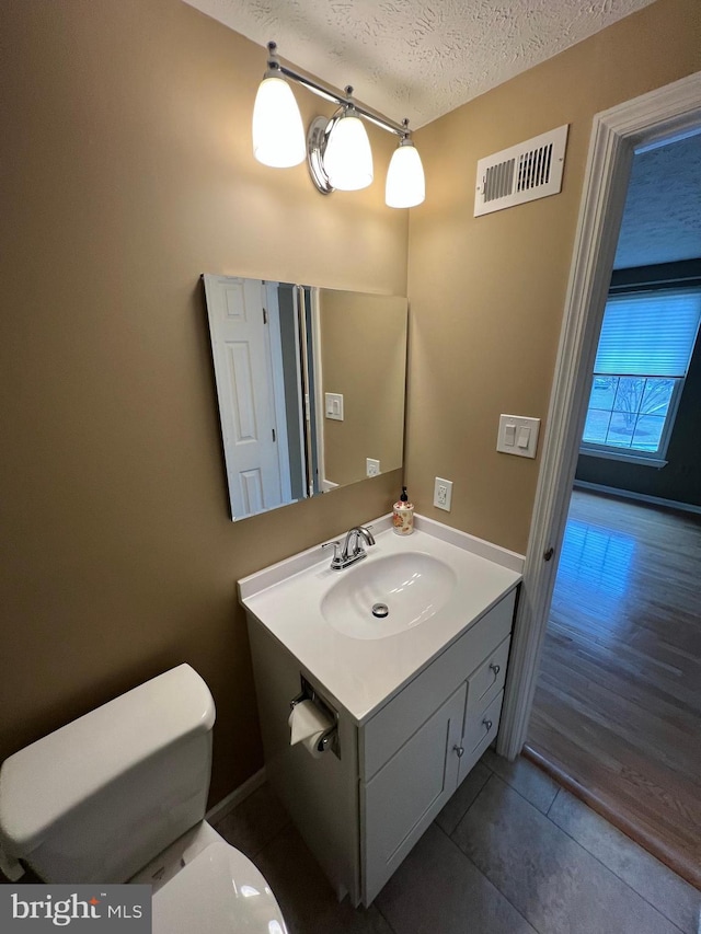 half bathroom featuring visible vents, toilet, a textured ceiling, vanity, and tile patterned floors