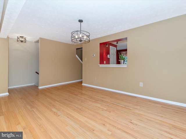 spare room with light wood-style flooring, baseboards, and a chandelier