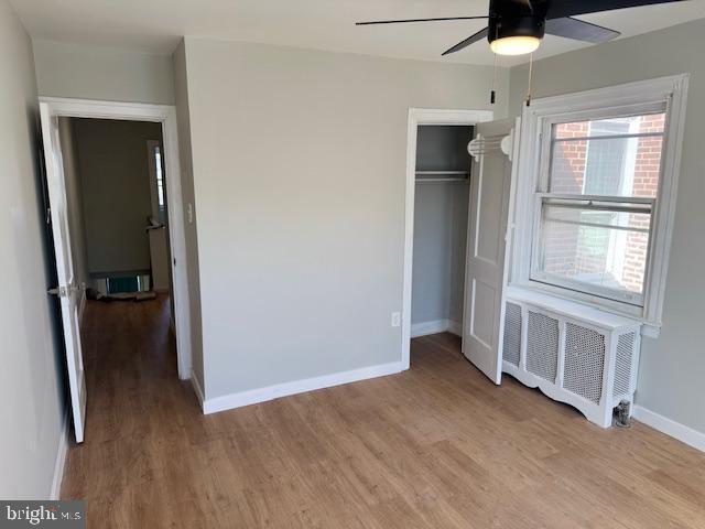 unfurnished bedroom with a closet, light wood-type flooring, radiator, and baseboards