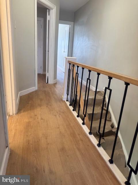 hallway with light wood-style floors, baseboards, and an upstairs landing