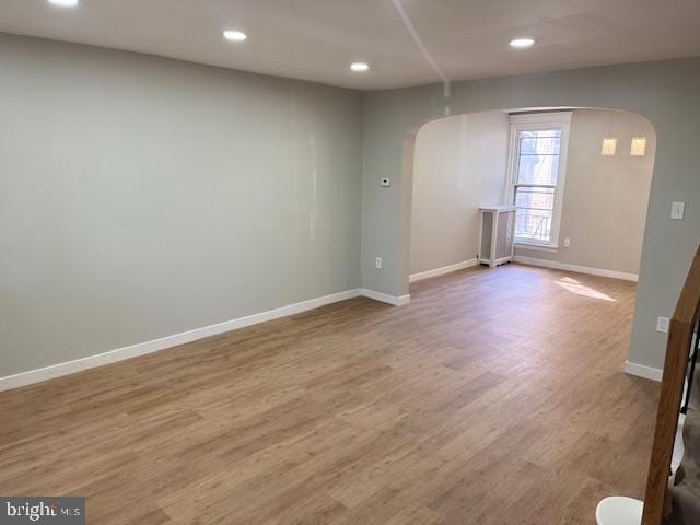 empty room featuring baseboards, arched walkways, wood finished floors, and recessed lighting