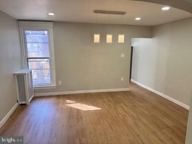 empty room with radiator heating unit, recessed lighting, wood finished floors, and baseboards