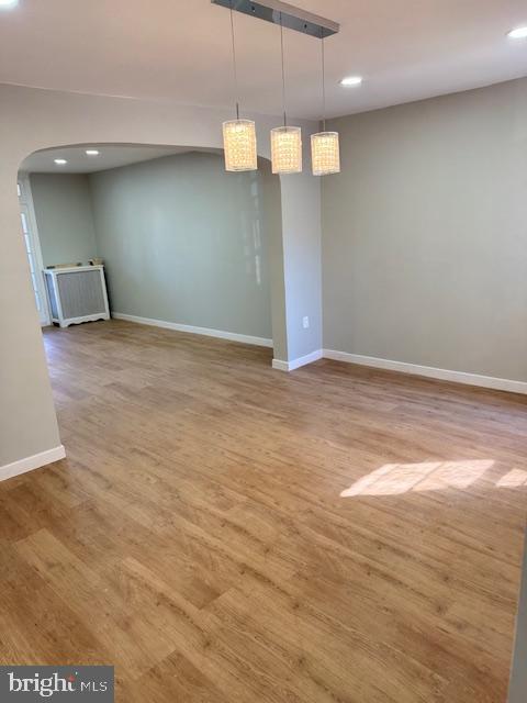 unfurnished room featuring arched walkways, recessed lighting, baseboards, and wood finished floors