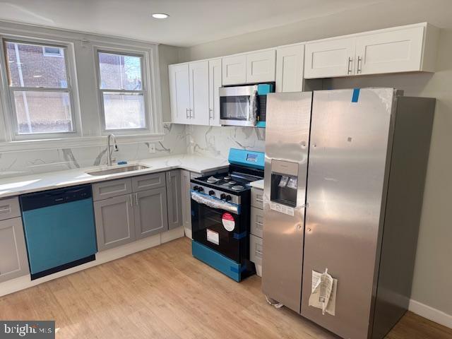 kitchen with light wood-style flooring, a sink, stainless steel appliances, light countertops, and backsplash