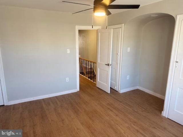 spare room featuring a ceiling fan, baseboards, arched walkways, and wood finished floors