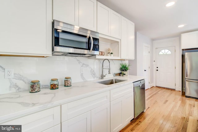 kitchen featuring light wood-style flooring, stainless steel appliances, a sink, white cabinetry, and tasteful backsplash