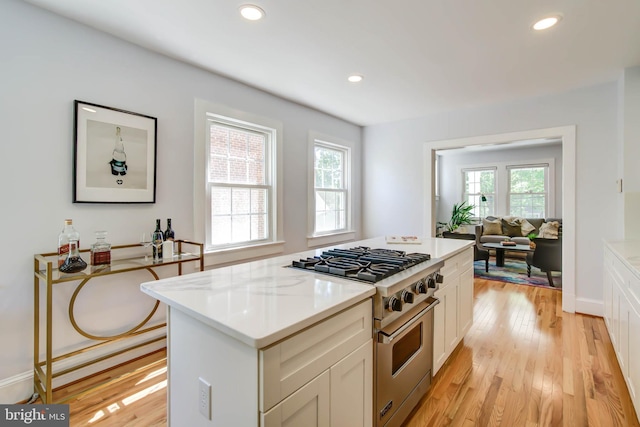 kitchen with light wood-style floors, high end stove, and a healthy amount of sunlight