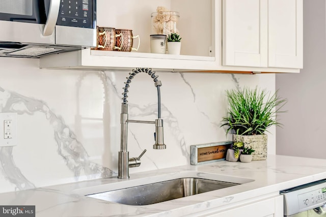 interior details with white cabinets, dishwashing machine, light stone counters, stainless steel microwave, and a sink