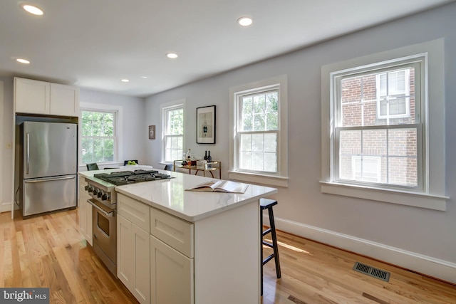 kitchen with stainless steel appliances, visible vents, white cabinets, a kitchen island, and light wood-type flooring