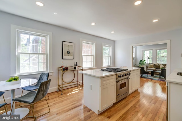 kitchen with light wood finished floors, stainless steel range, white cabinetry, and recessed lighting