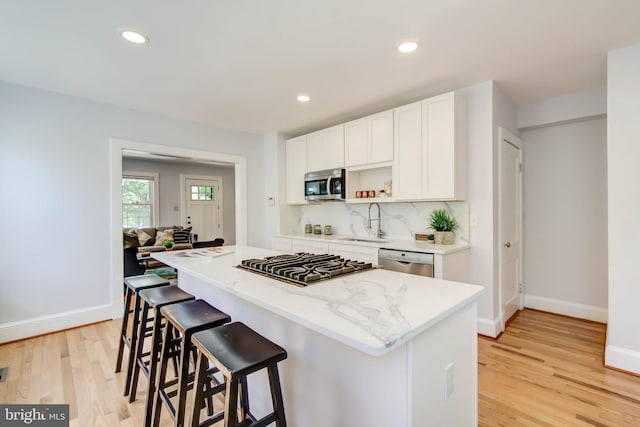 kitchen featuring a sink, appliances with stainless steel finishes, light wood-type flooring, a center island, and tasteful backsplash