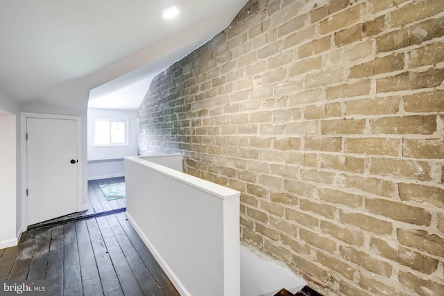 hallway featuring vaulted ceiling, brick wall, dark wood-type flooring, and an upstairs landing