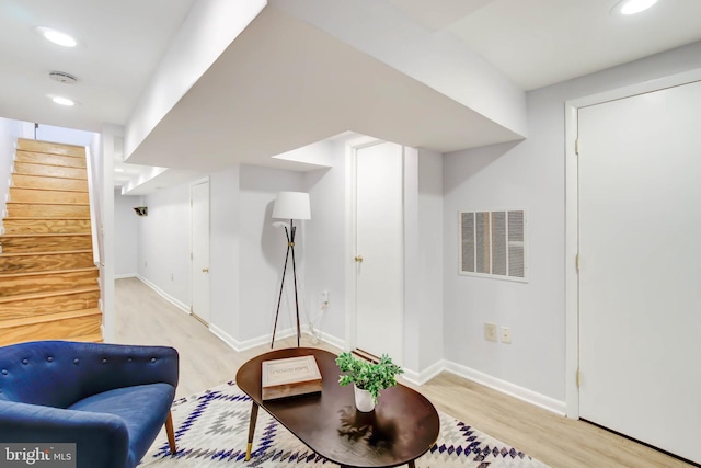 sitting room with light wood-type flooring, visible vents, baseboards, and stairs