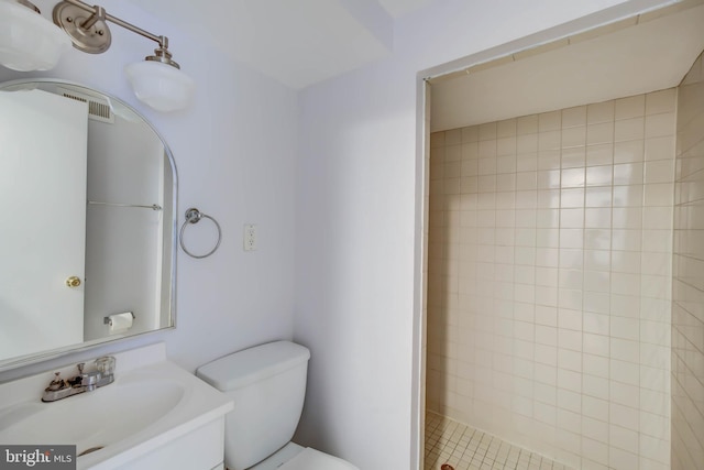 bathroom featuring vanity, a tile shower, and toilet