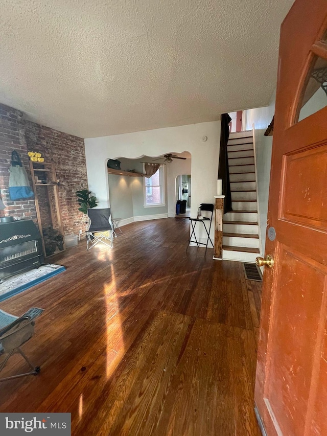 unfurnished living room with visible vents, arched walkways, stairway, wood finished floors, and a textured ceiling