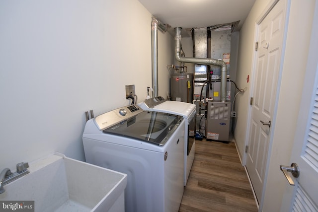 clothes washing area featuring water heater, washing machine and dryer, a sink, wood finished floors, and laundry area