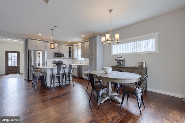 dining area with a notable chandelier, a healthy amount of sunlight, dark wood-style flooring, and baseboards