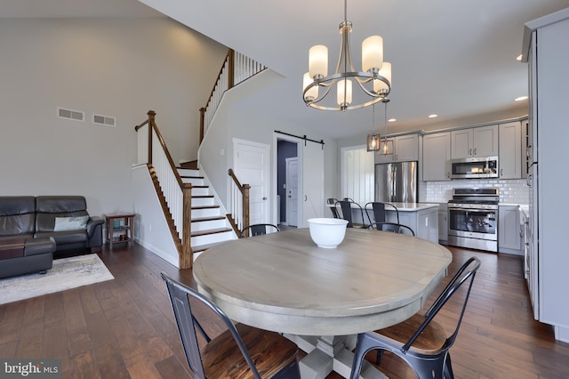 dining room with stairway, visible vents, dark wood finished floors, an inviting chandelier, and a barn door