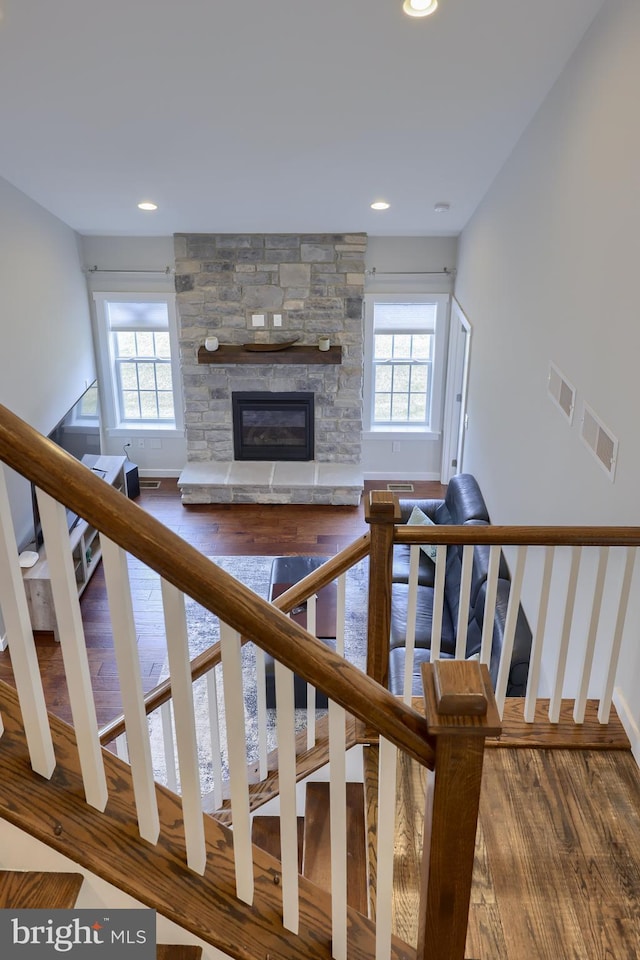 staircase with a stone fireplace, recessed lighting, wood finished floors, and visible vents