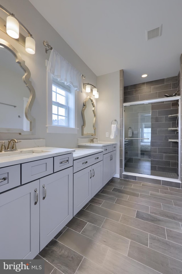 full bathroom featuring a sink, visible vents, two vanities, and a stall shower